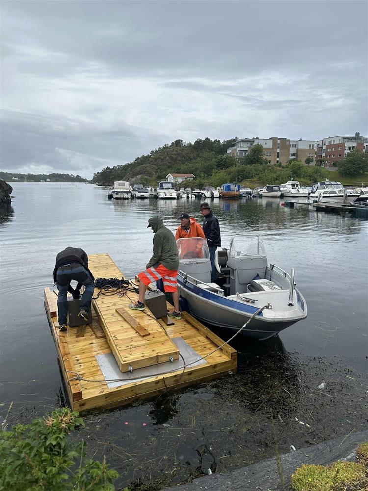 Flytebryggen monteres av to menn. To menn i en båt på siden - Klikk for stort bilde
