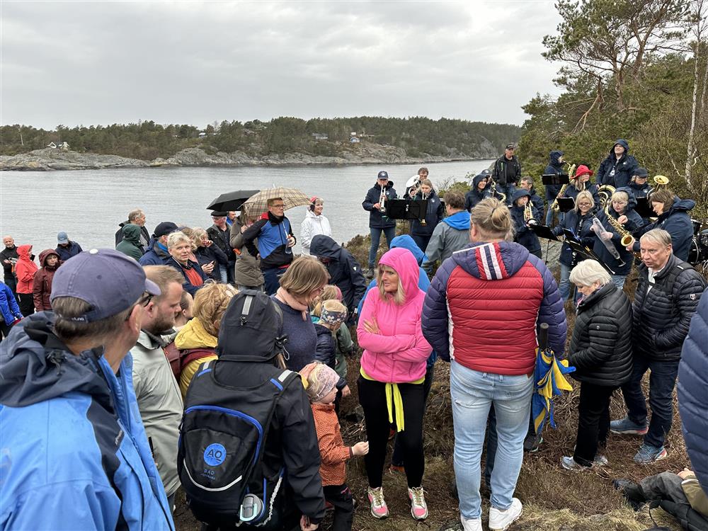 Mange mennesker samlet i området ved dagsturhytta, sjøen ligger vakkert bak dem. - Klikk for stort bilde