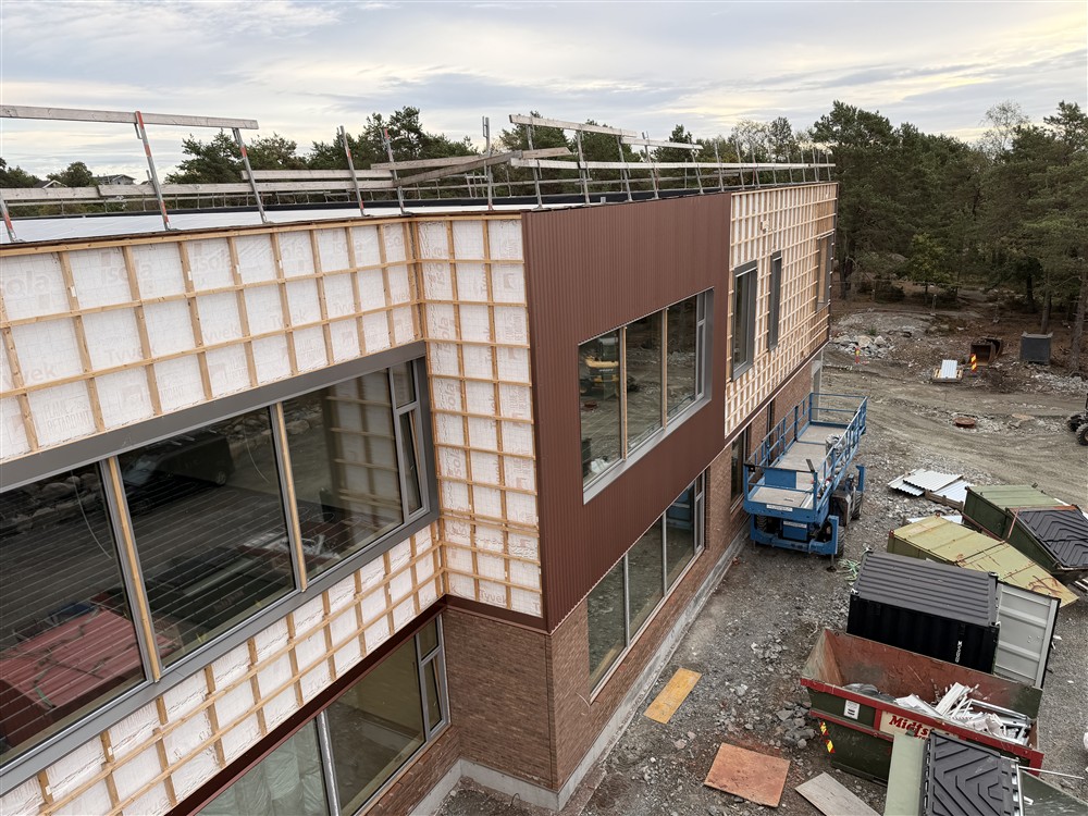 Et skolebygg under oppføring, materialer mm. på bakken.  - Klikk for stort bilde