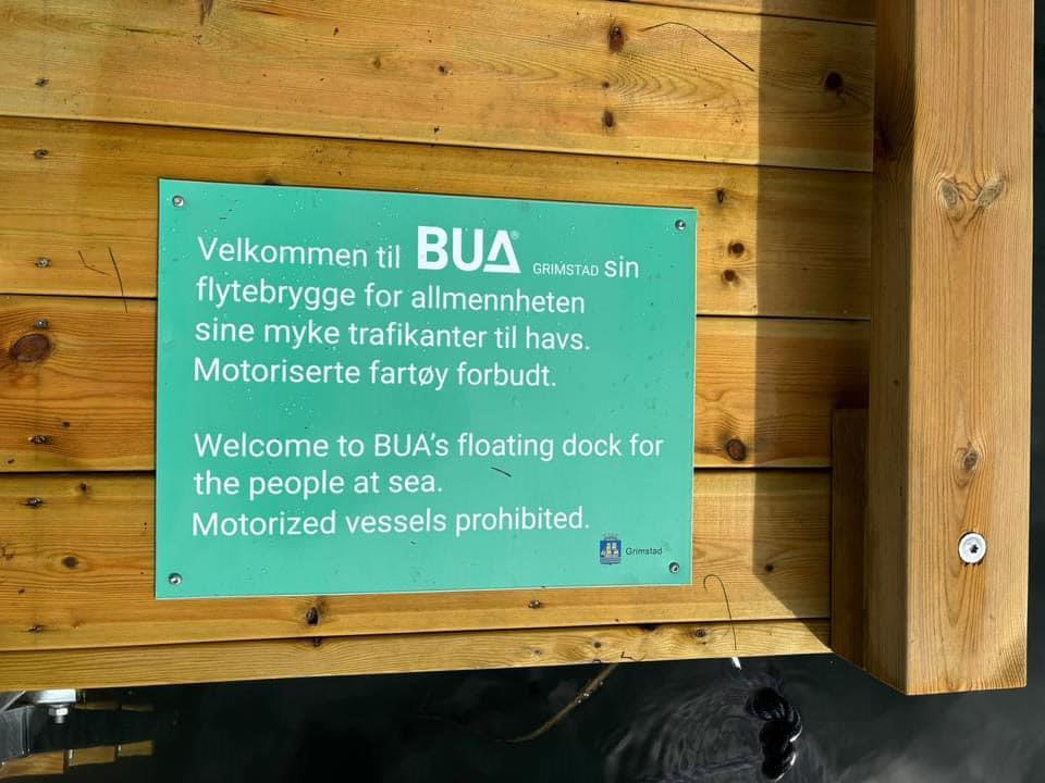 Grønt skilt som er festet på flytebrygga. Det sier Velkommen til BUA sin flytebrygge og at den er for myke trafikanter og ikke motoriserte fartøy. Tekst er også på engelsk. - Klikk for stort bilde