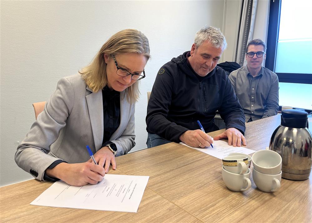 Beate Skretting og Rolf Olsen sitter ved et bord. begge skriver under på hver sin kontrakt. - Klikk for stort bilde