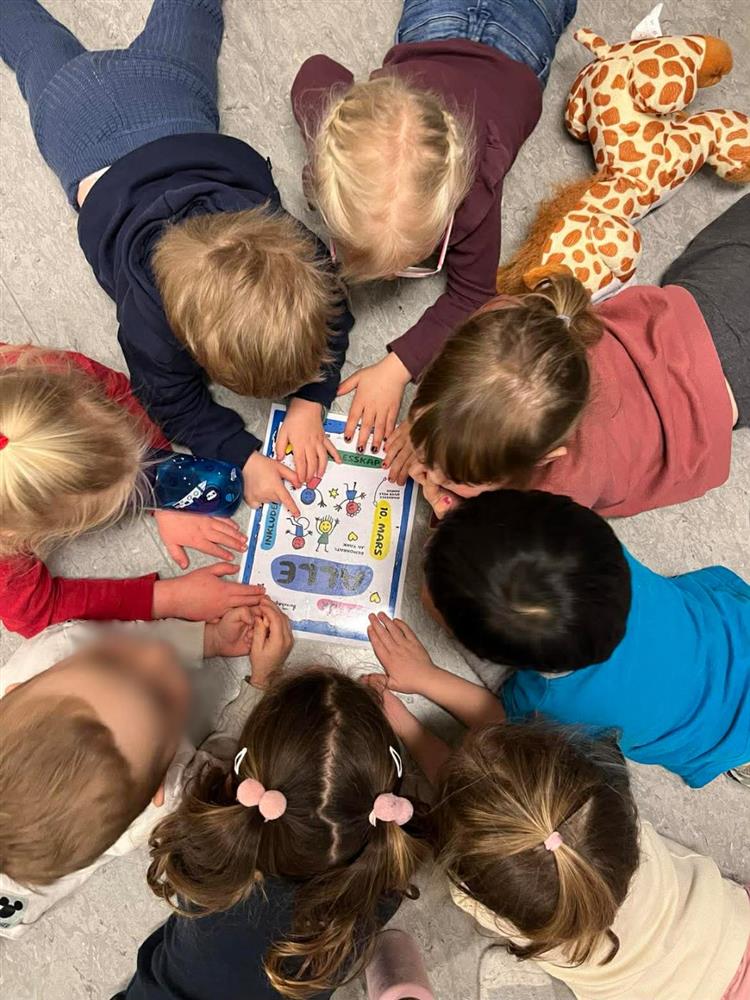 Bilde ovenfra av åtte barn som ligger på gulvet og jobber med oppgaver på et ark - Klikk for stort bilde