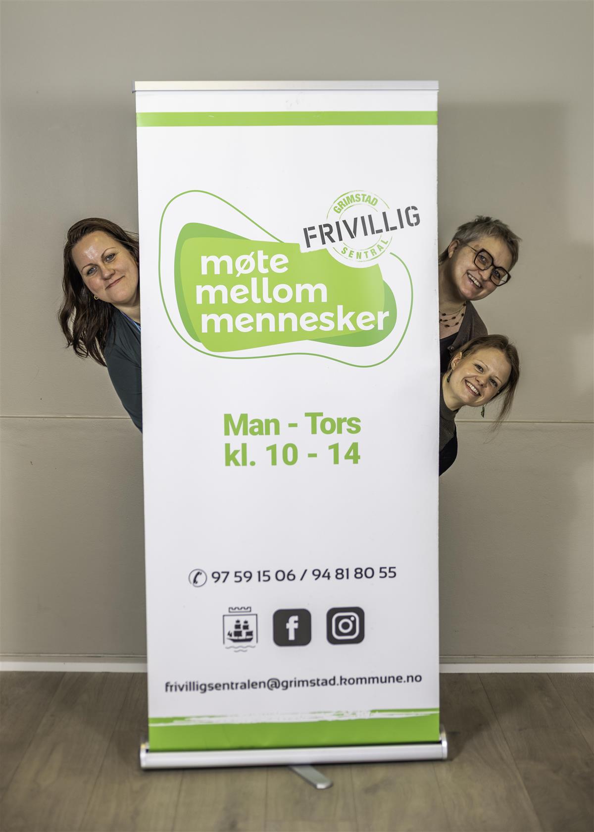 Roll up for Frivilligsentralen, tre damer står bak den, men stikker hodet frem - Klikk for stort bilde