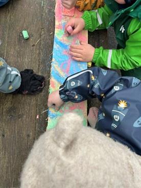 Barnehender som lager kunstverk på en planke med kritt - Klikk for stort bilde