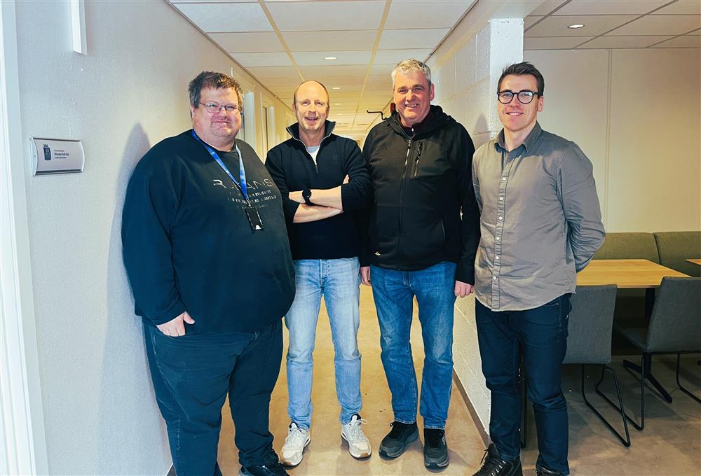 Fire menn står oppstilt i en gang og smiler til kamera. F.v. Lars Ole Hansen, Arve Falk Lorentzen, Rolf Olsen og Halvard Hinlo - Klikk for stort bilde