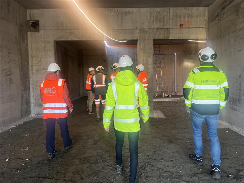 Mennesker med verneutstyr på vei inn i et bygg som foreløpig består av betongvegger - Klikk for stort bilde