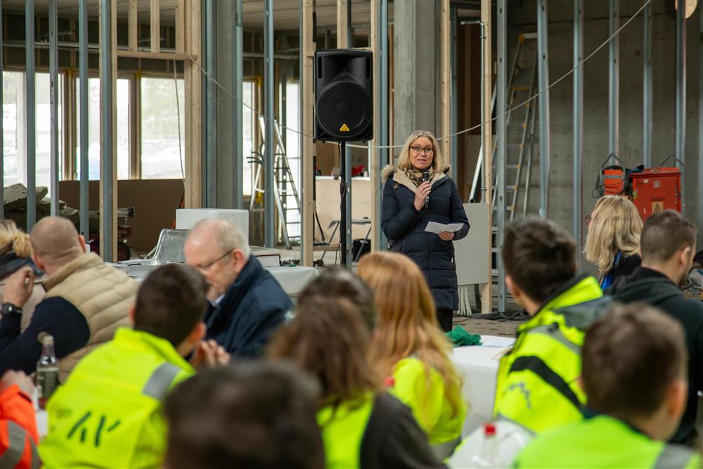 Beate Skretting prater i mikrofon til arbeiderne inne på det soms kal bli nye Fjære barneskole.  - Klikk for stort bilde